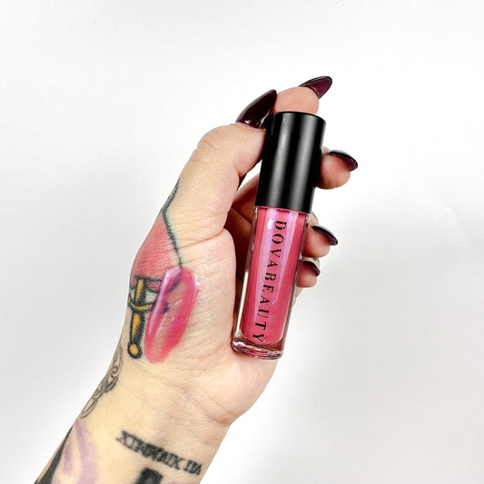 hand holding pink lip gloss with swatch of gloss on hand